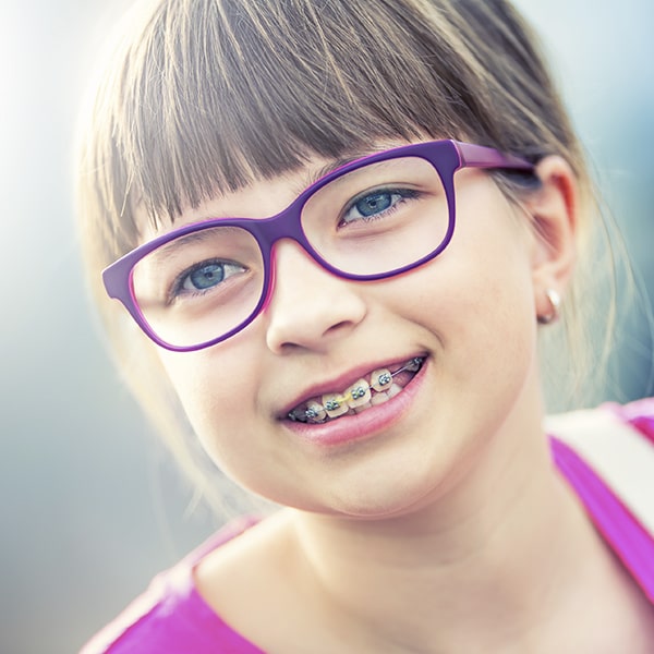 A girl with braces and glasses smiling