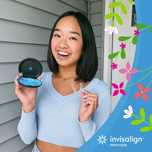A smiling girl is holding invisalign in her left hand and invisalign case at her right