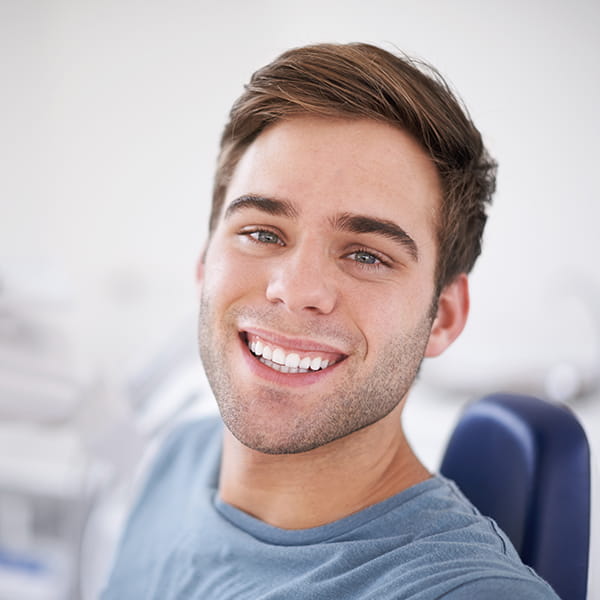 A smiling man wearing a gray shirt is seated on a dental chair